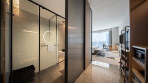 Ett modernt hotellrum med en glasvägg, en rund lampa, en platt-TV och en sittgrupp med soffa och soffbord.
