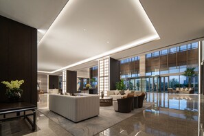 Un'ampia hall con un design moderno, caratterizzata da una grande area relax, una reception e grandi finestre con vista sull'esterno.