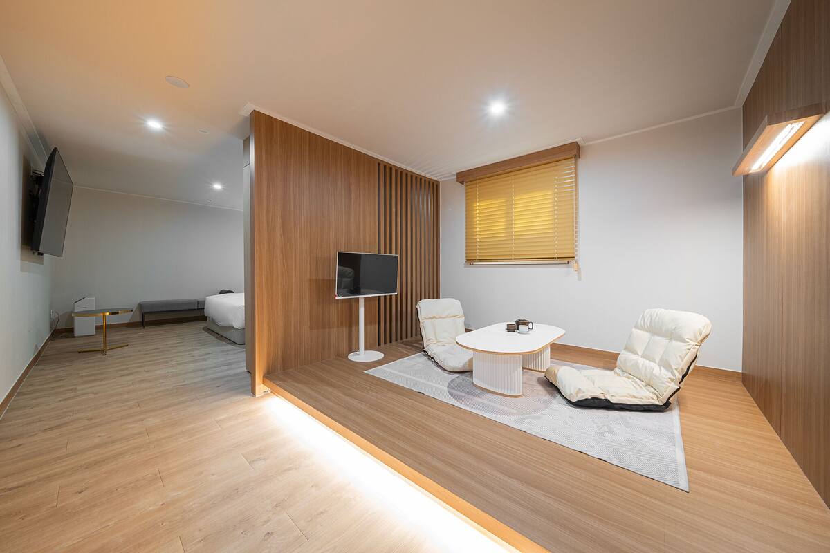 A modern living room with a sofa, two armchairs, a coffee table, a flat-screen TV, and a wooden accent wall.