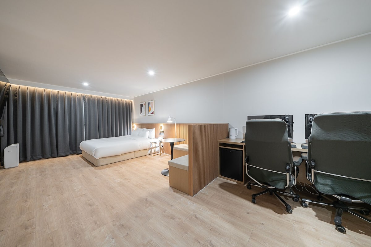 A modern hotel room with a bed, desk, chairs, and a small kitchenette.