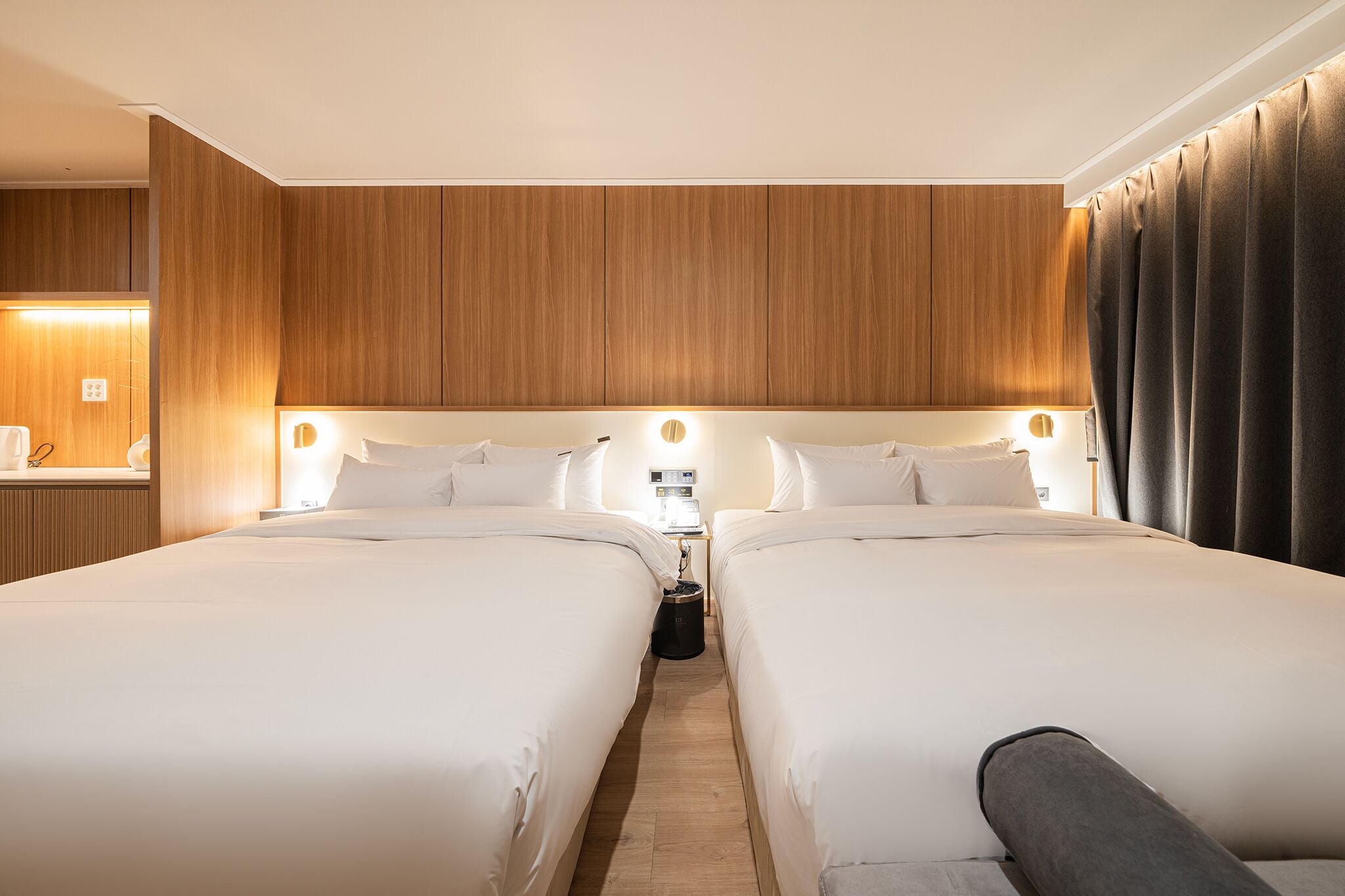 Une chambre d’hôtel avec deux lits, des lambris en bois aux murs, une table de chevet avec une lampe et une fenêtre avec des rideaux.