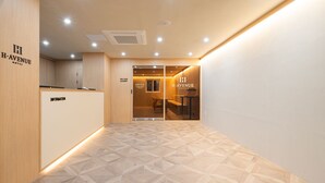 A hotel reception area with a geometric patterned floor, a reception desk, and a self-service bar and laundry area. - Cheonan H-Avenue Cheonan Buldang (Cheonan)