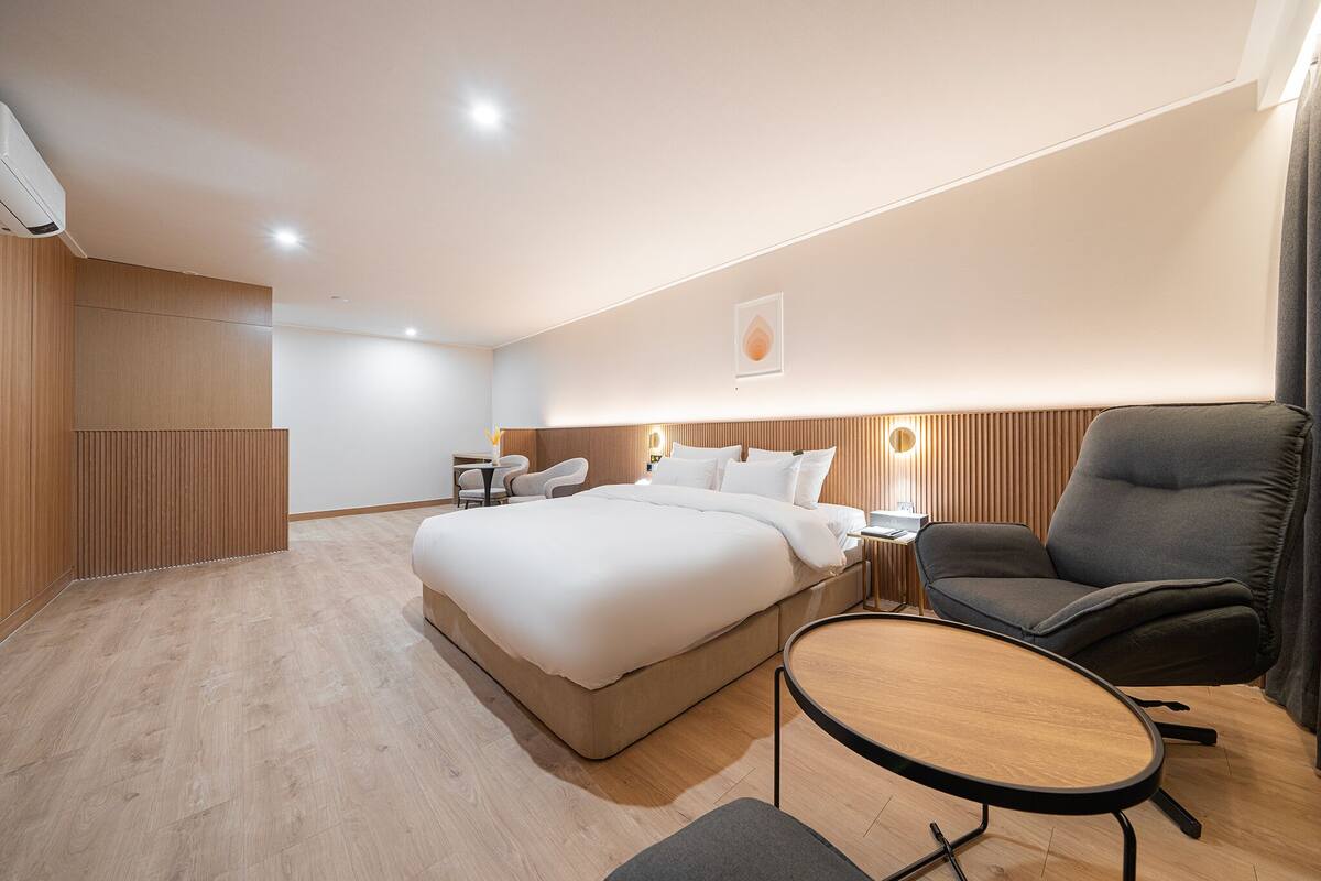 A modern hotel room with a large bed, a desk, a chair, and a small round table.