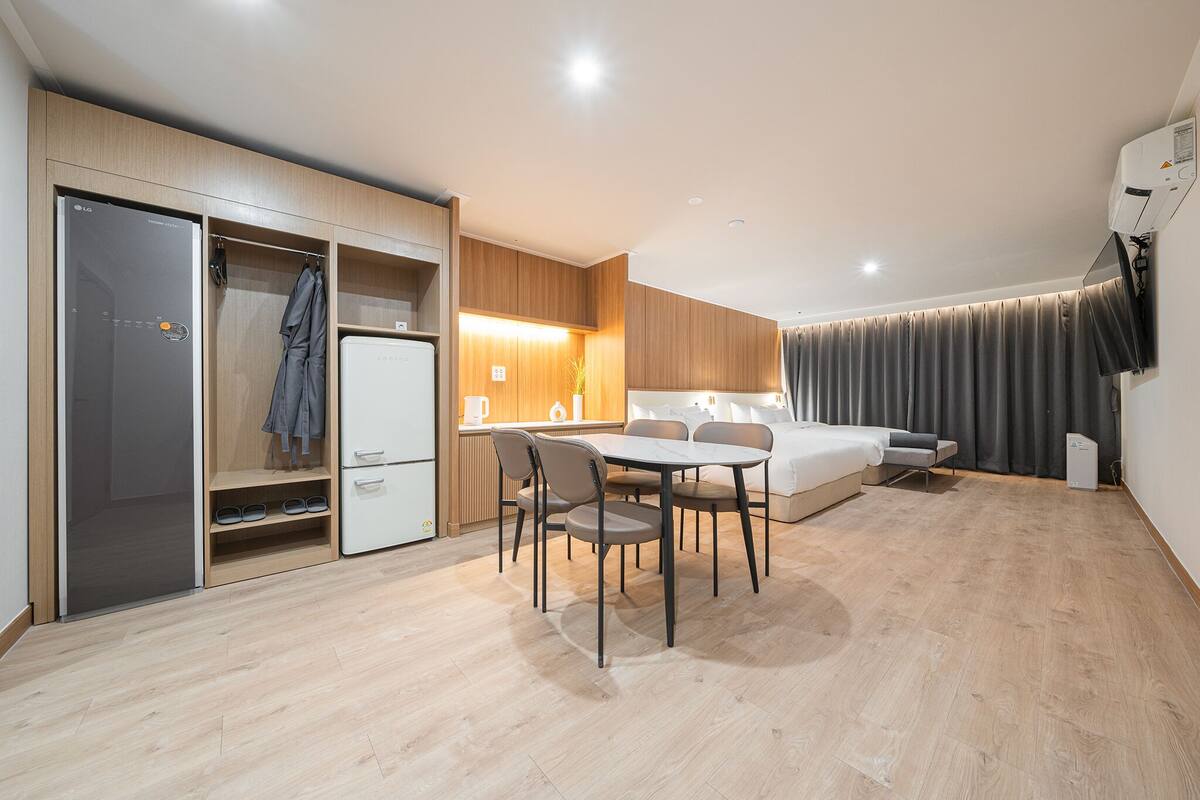 A modern hotel room with a dining area, a wardrobe, a bed, and a built-in air conditioning unit.