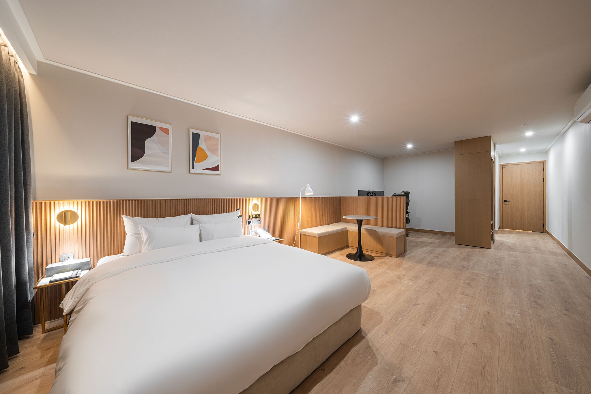 Una habitación de hotel moderna con una cama grande, mesitas de noche, un escritorio y una pequeña zona de estar.