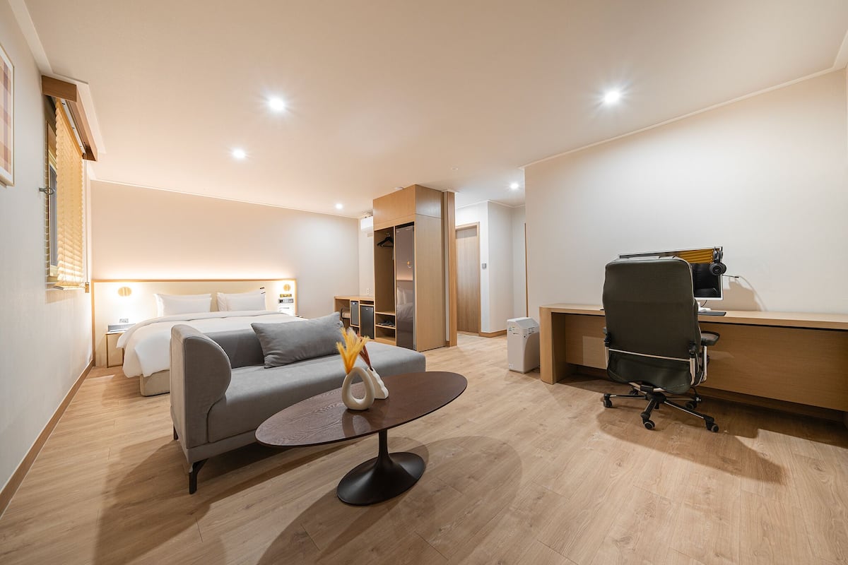 A modern hotel room with a bed, a sofa, a desk, and a chair.