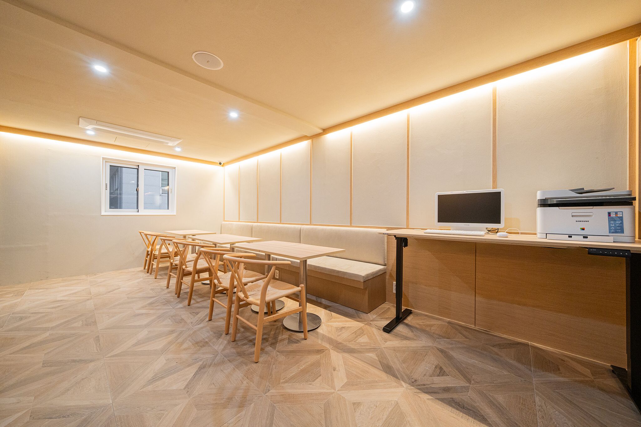 Una sala de reuniones moderna con una mesa larga, sillas, un banco, una computadora e impresora.