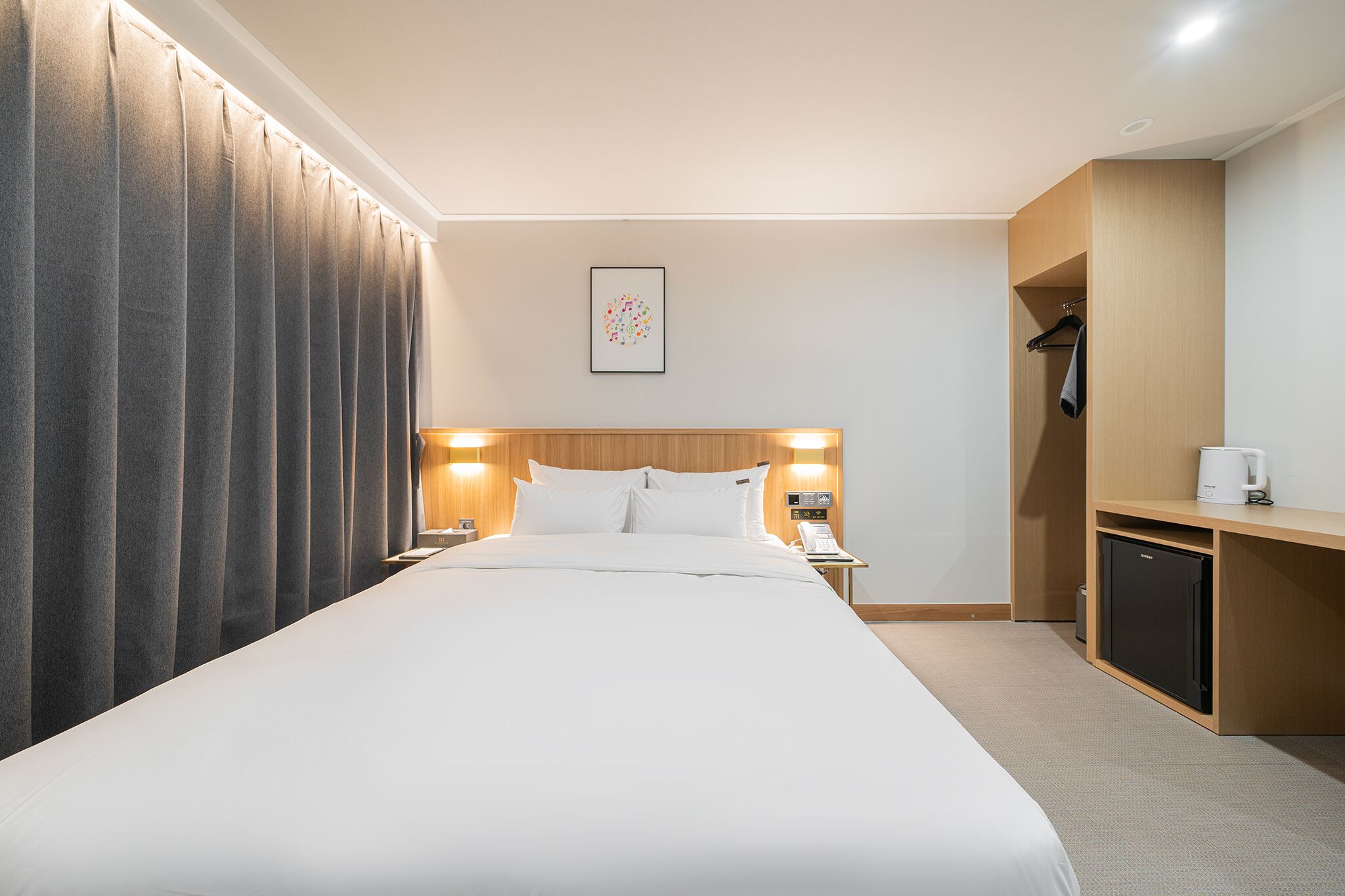 Une chambre d’hôtel avec un grand lit, des lampes de chevet, un petit bureau avec une machine à café et une armoire.