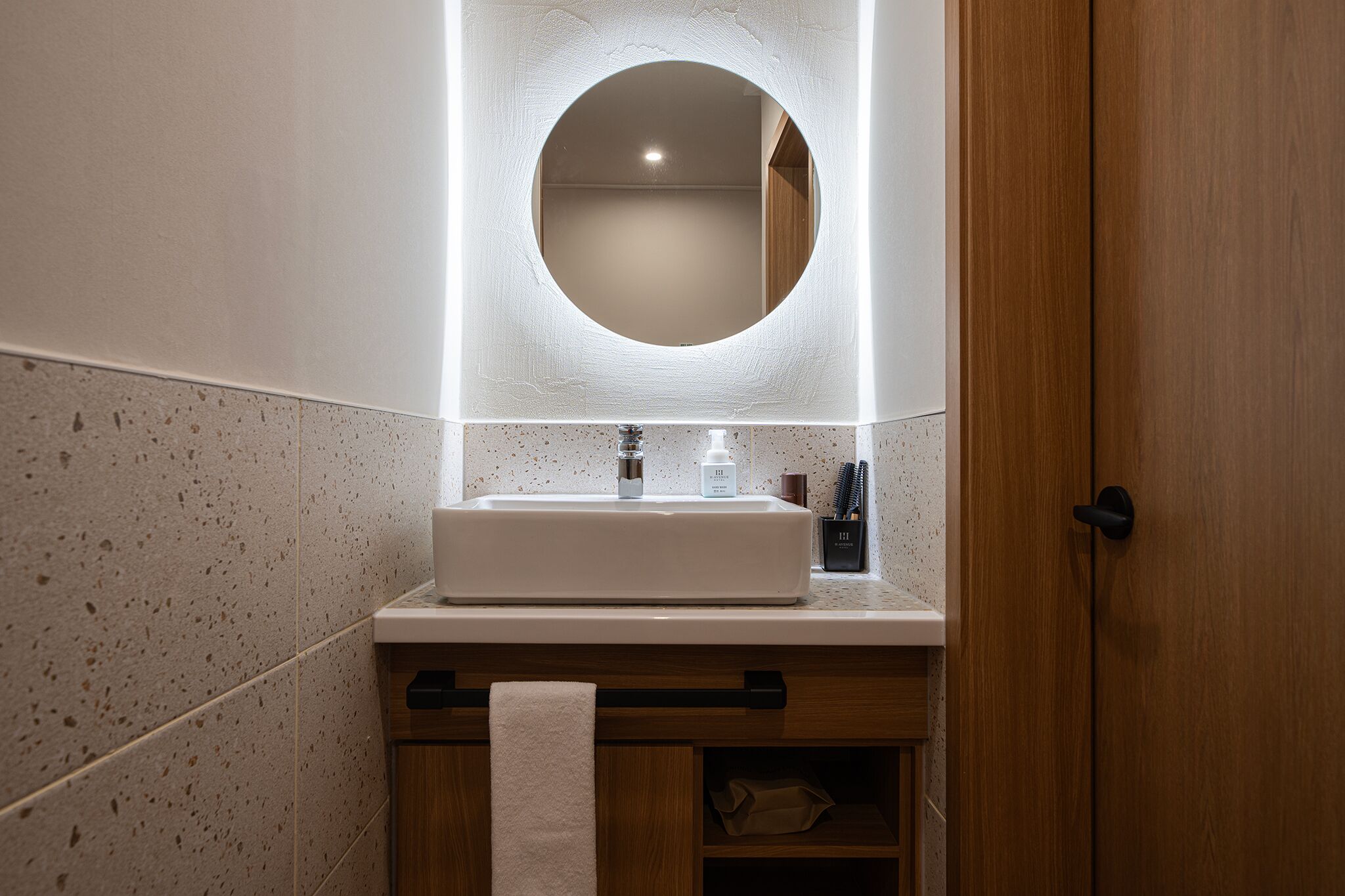 Un baño con un espejo redondo, un lavamanos blanco y un perchero para toallas.