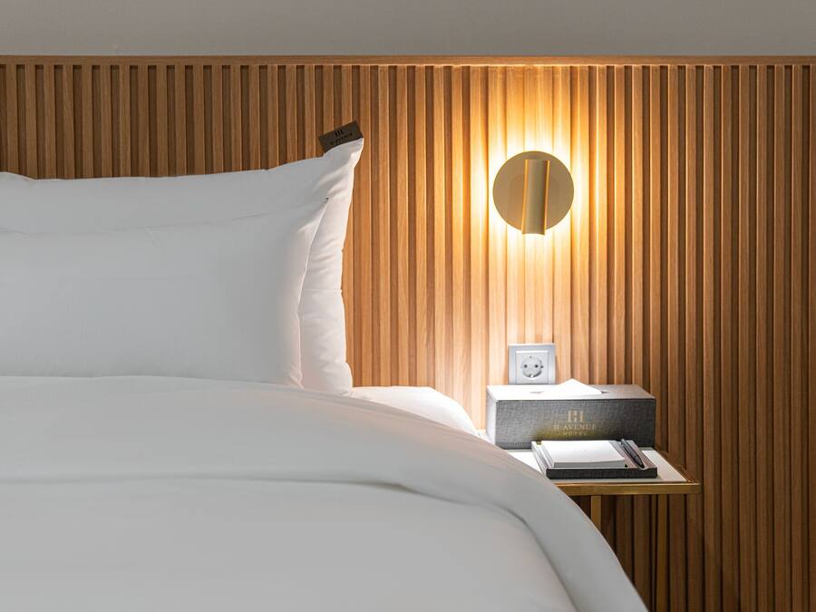 A neatly made bed with white linens, a wooden slatted headboard, a bedside table with a lamp, and a small box labeled "Haven Hotel."