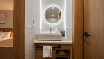 Un baño con tocador de madera, lavamanos blanco y espejo redondo.