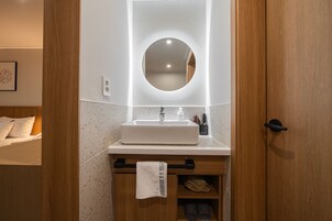 Un baño con tocador de madera, lavamanos blanco y espejo redondo.