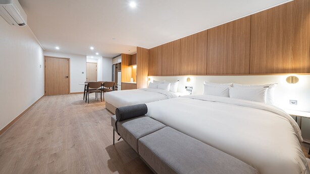 A modern hotel room with two beds, a wooden accent wall, a desk with a chair, and a bench. - Cheonan H-Avenue Cheonan Buldang (Cheonan)