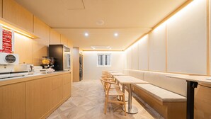 A modern kitchen with wooden cabinets, a built-in oven, and a long counter with a coffee machine. There are wooden chairs and a bench along the counter. - Cheonan H-Avenue Cheonan Buldang (Cheonan)