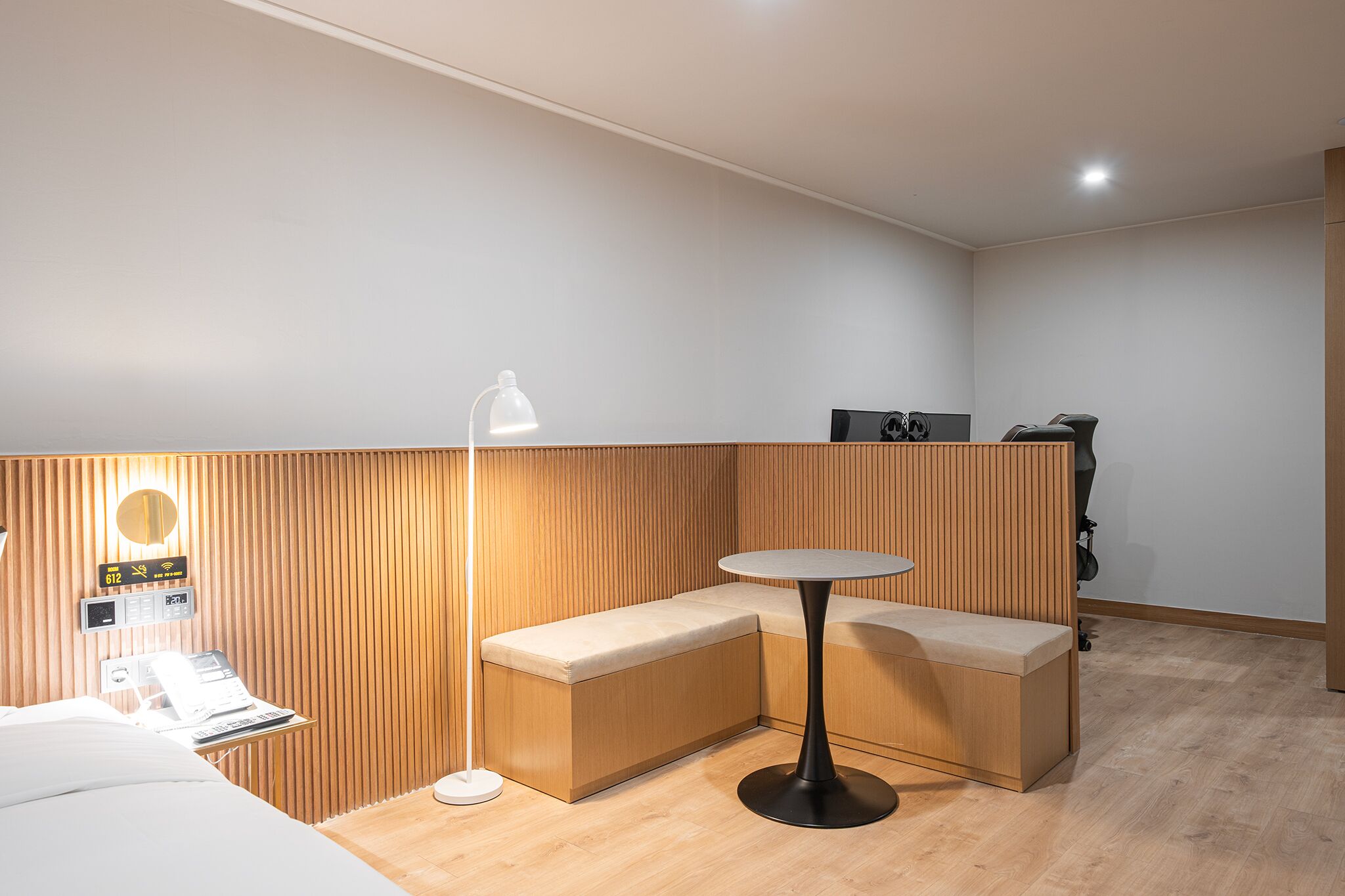 Una habitación de hotel moderna con un panel de pared de madera, una mesa redonda, un sofá y un escritorio con una lámpara.