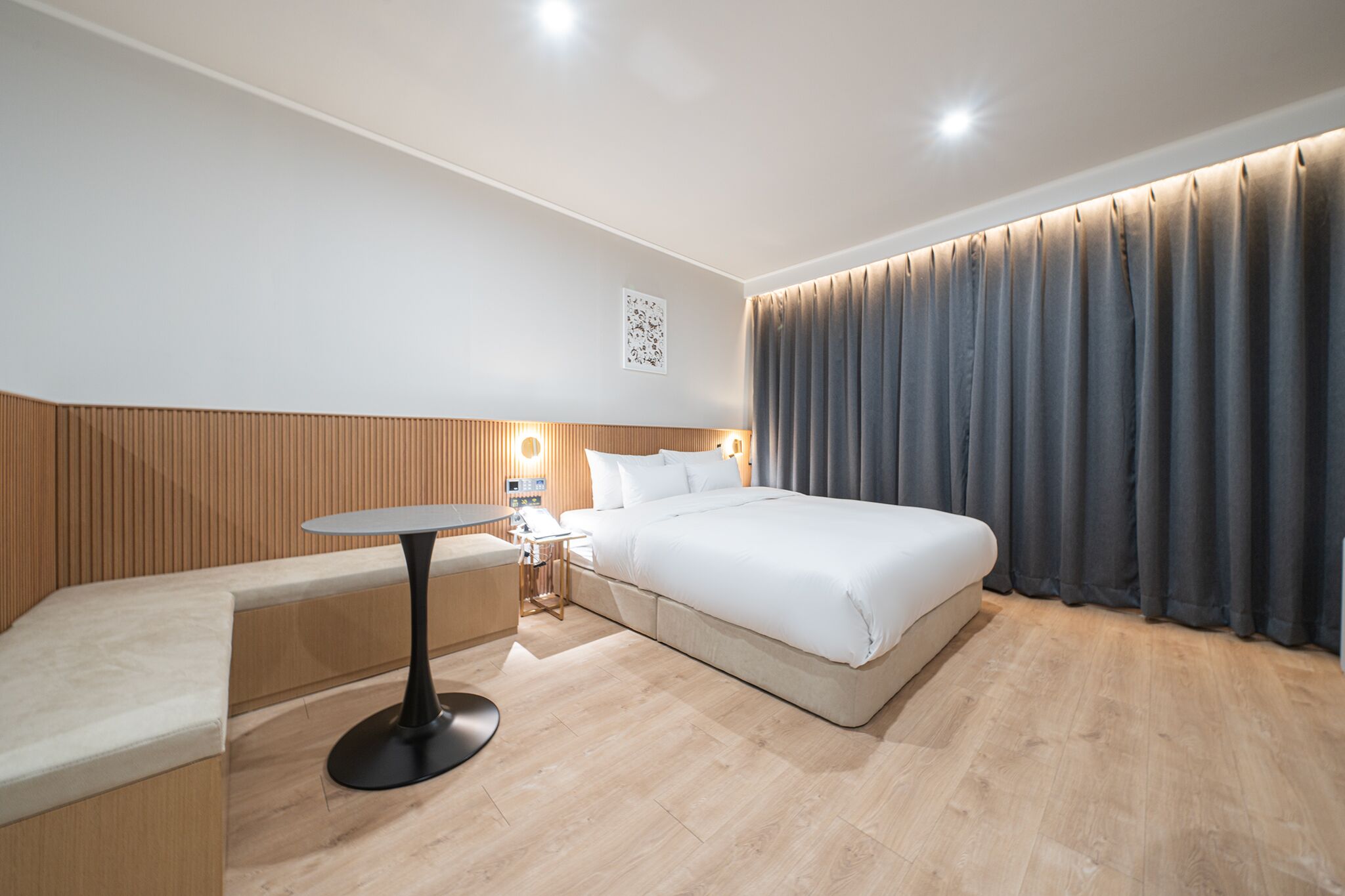 Ein modernes Hotelzimmer mit einem Bett, einem kleinen Tisch, einer Bank und einem Nachttisch mit einer Lampe.