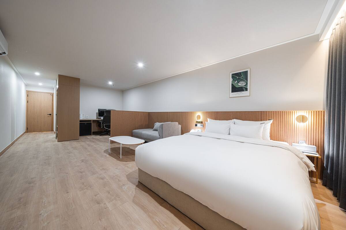 A modern hotel room with a large bed, a desk, a chair, and a small table.