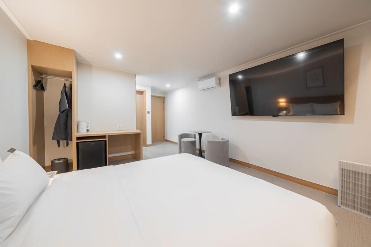 Habitación de hotel con una cama grande, un escritorio, una silla, una mesita, un espejo y un armario.