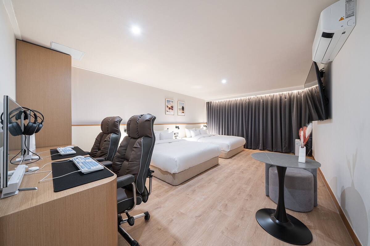 A hotel room with a desk, two chairs, a bed, a small table, and a TV mounted on the wall.
