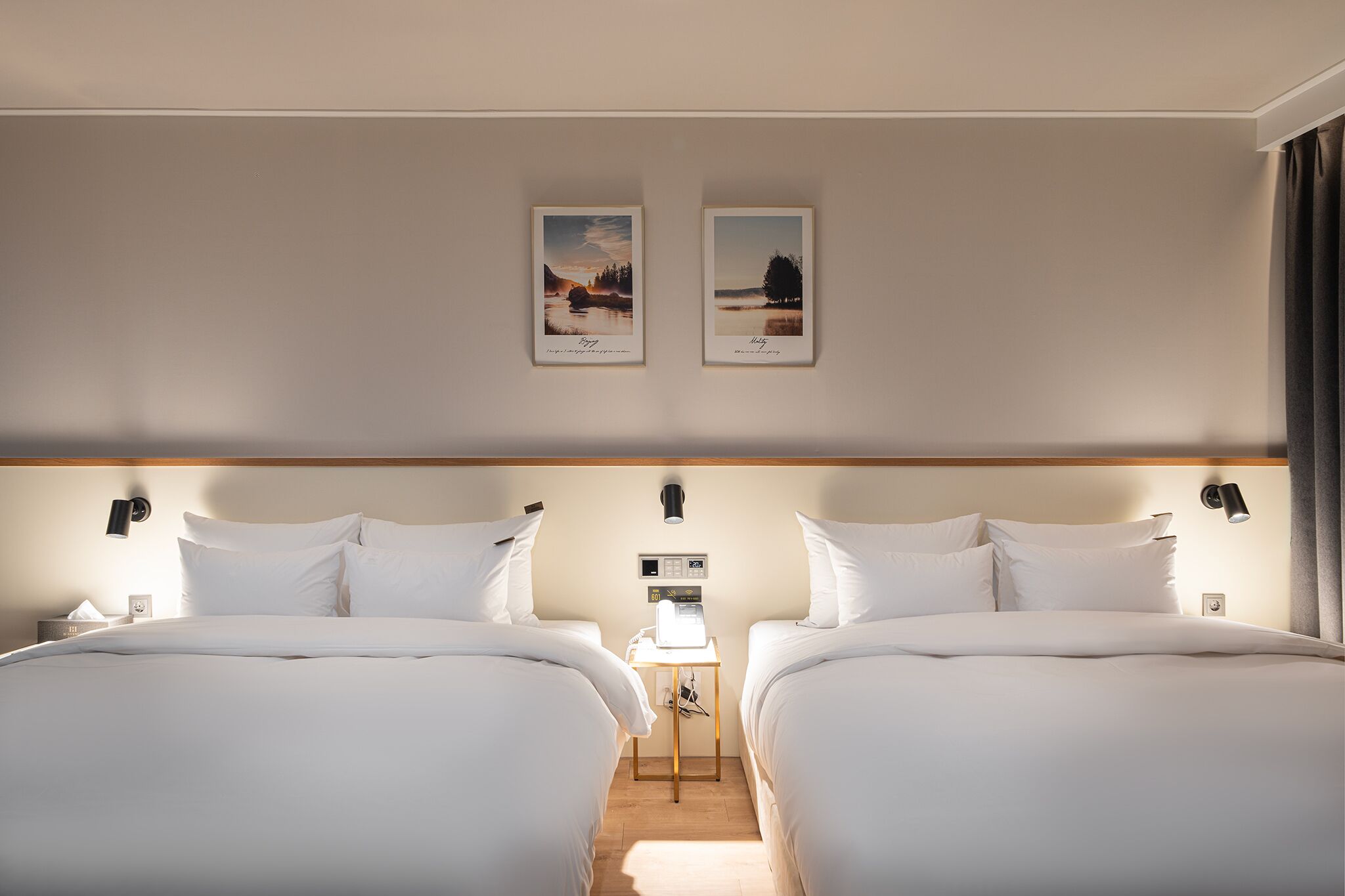 Habitación de hotel con dos camas, una mesita de noche, una lámpara y dos cuadros en la pared.