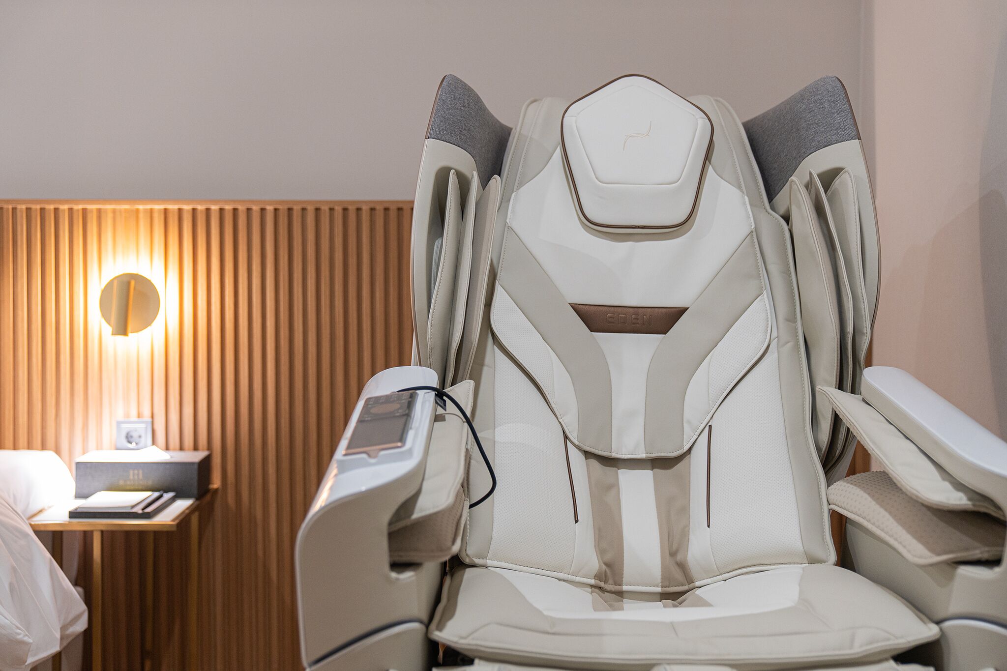 A massage chair in a room with a wooden panel wall and a bedside table with a lamp.