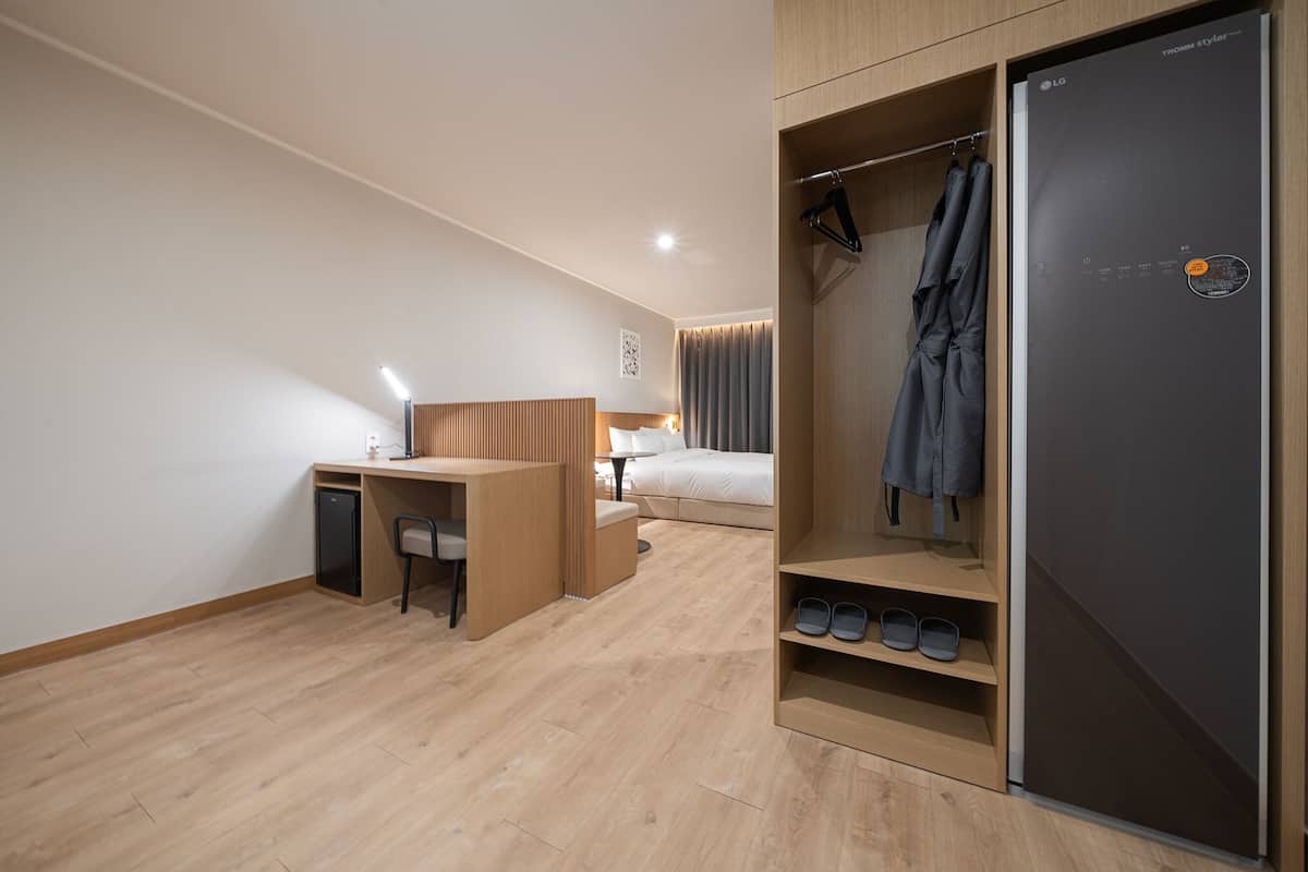 A modern hotel room with a wooden desk, a bed, a wardrobe, and a built-in shoe rack.