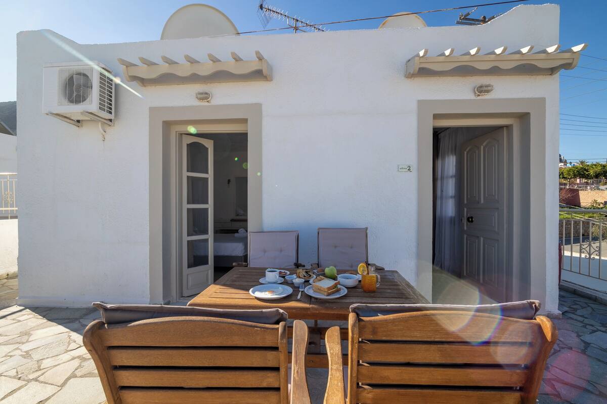 A table set for two with a white exterior wall, two doors, and an air conditioning unit.