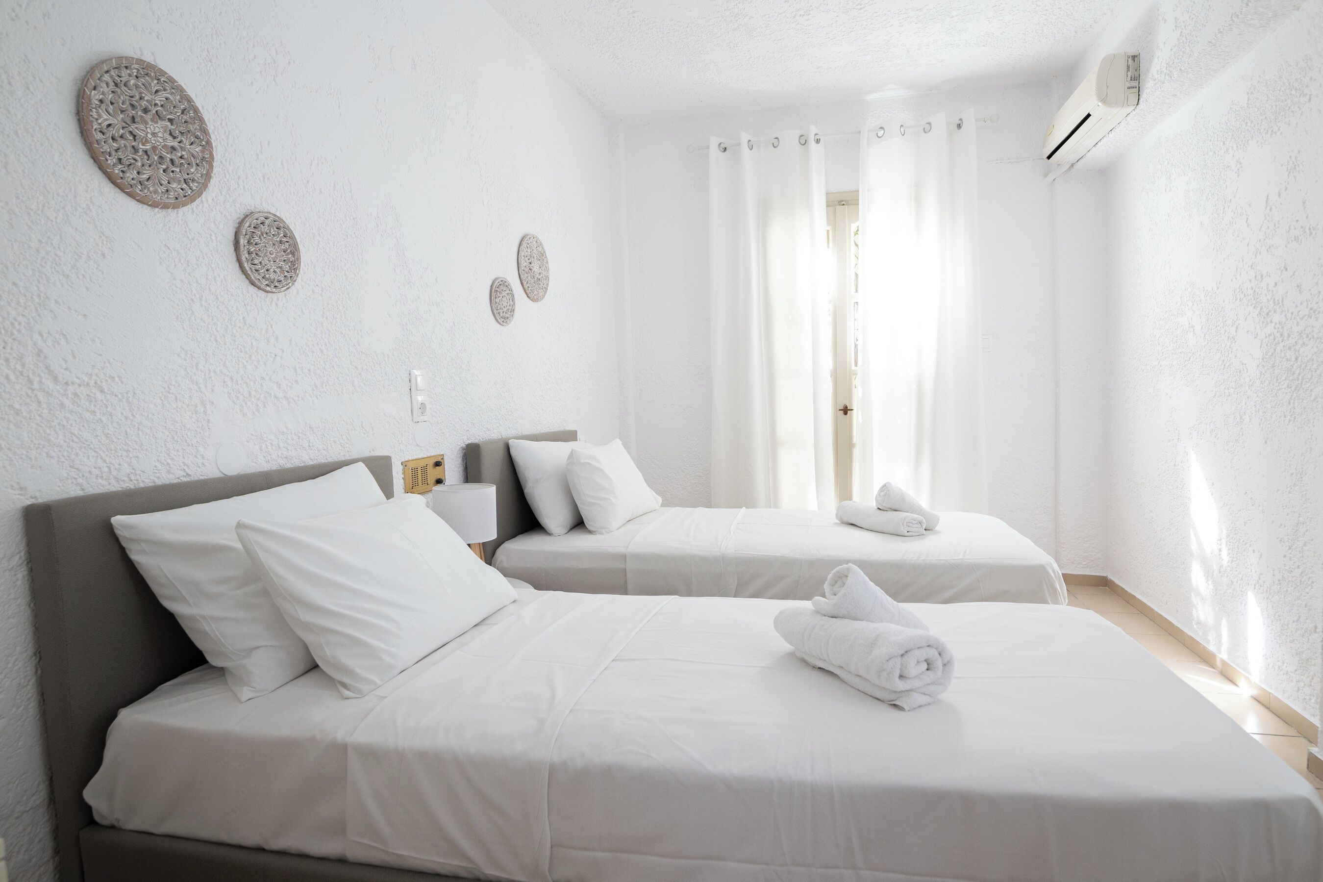 A hotel room with two beds, white bedding, a nightstand with a lamp, and decorative wall plates.