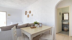 Una habitación de paredes blancas con una mesa de comedor, sillas, un sofá y una planta pequeña.