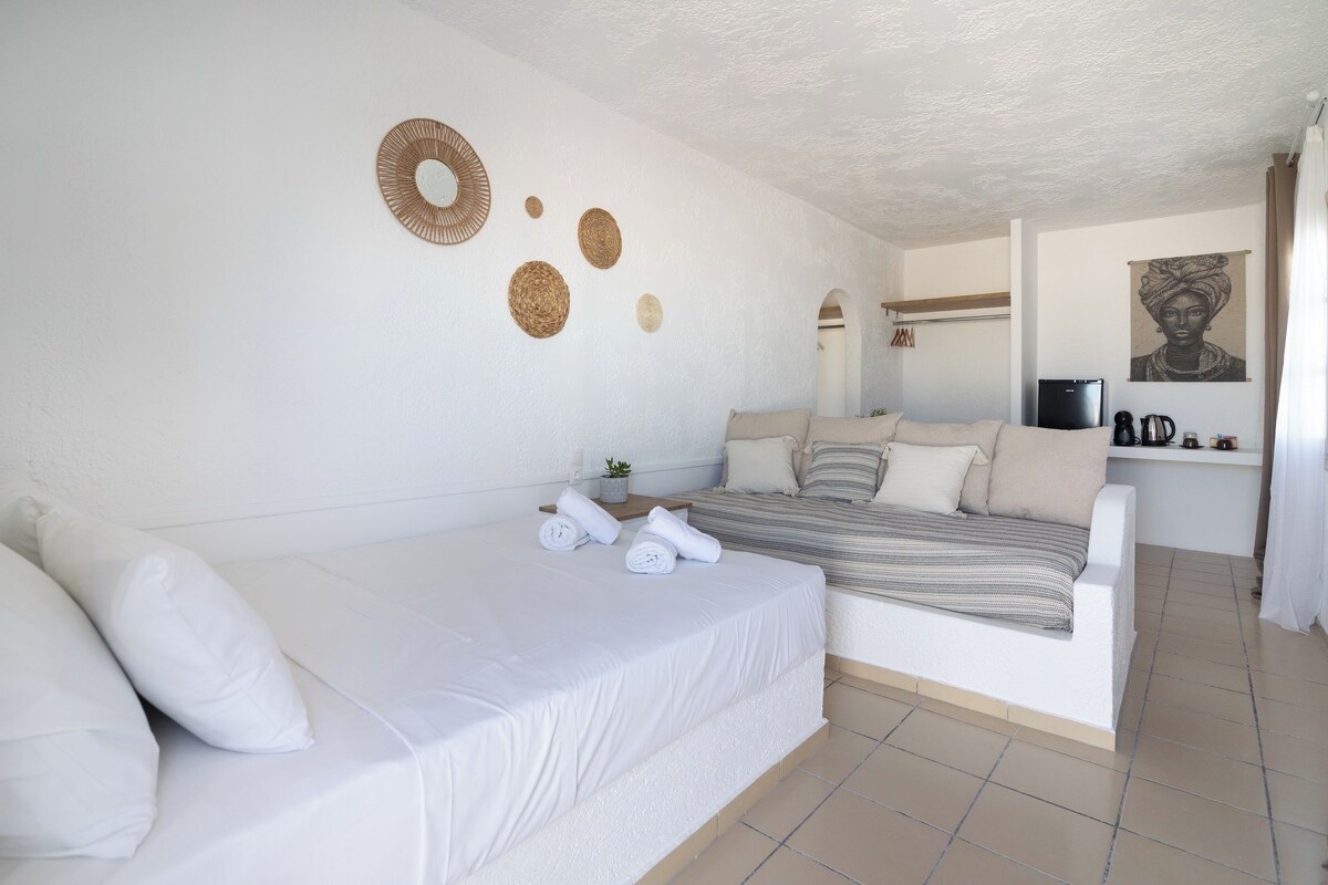 A bedroom with a bed, a sofa, a small table with a plant, and a wall with decorative items.