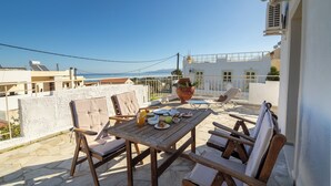 Una mesa de madera con sillas y una planta en maceta en una terraza en la azotea, con vista al mar.