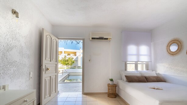 Un dormitorio con cama, una mesita de noche, una pequeña planta en maceta y una ventana con persianas.
