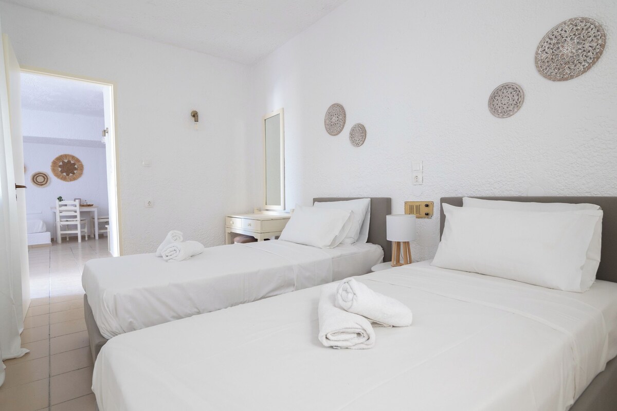 A hotel room with two beds, white bedding, a desk, a chair, and decorative wall art.