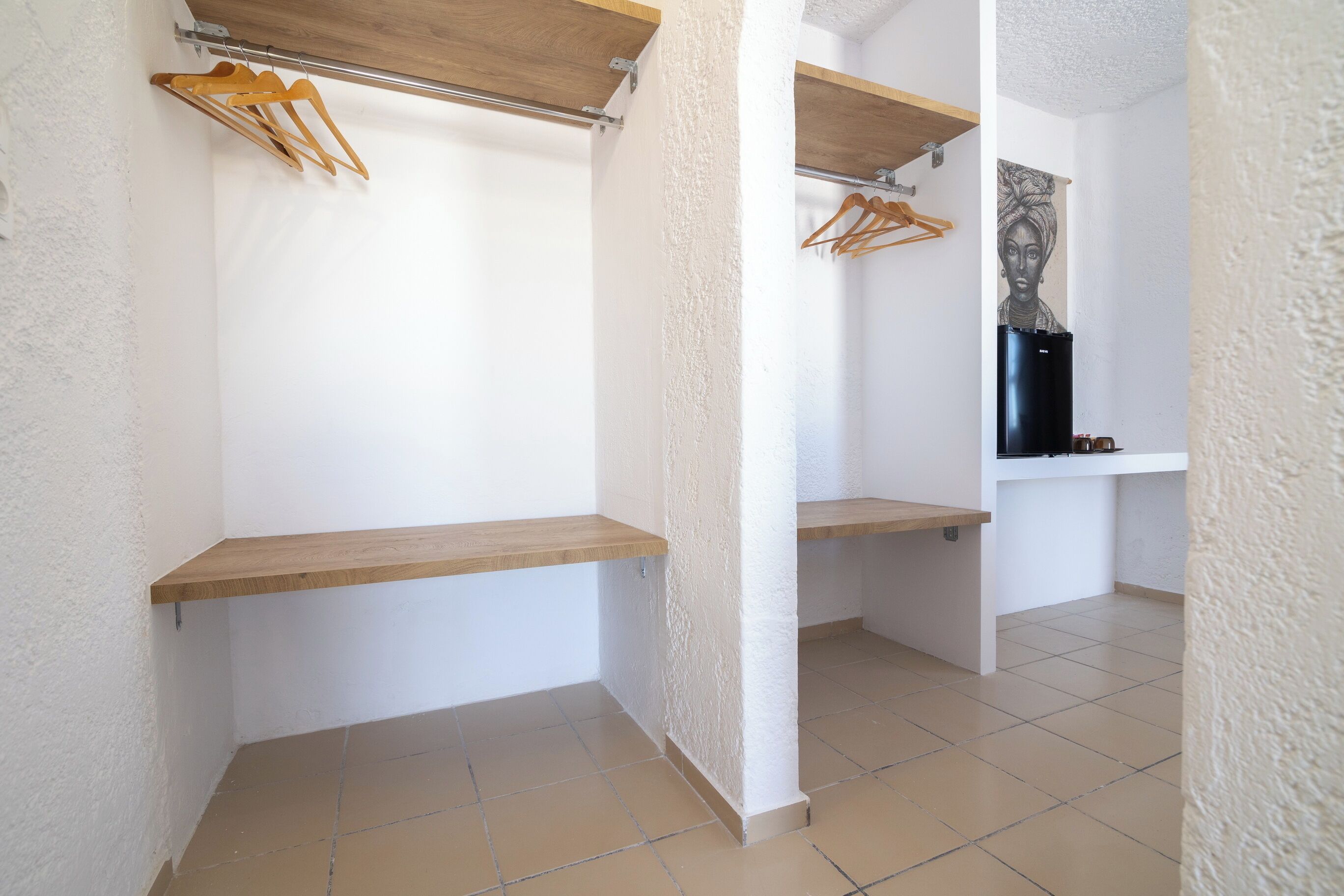 A room with a white textured wall, a wooden shelf, and a black refrigerator.