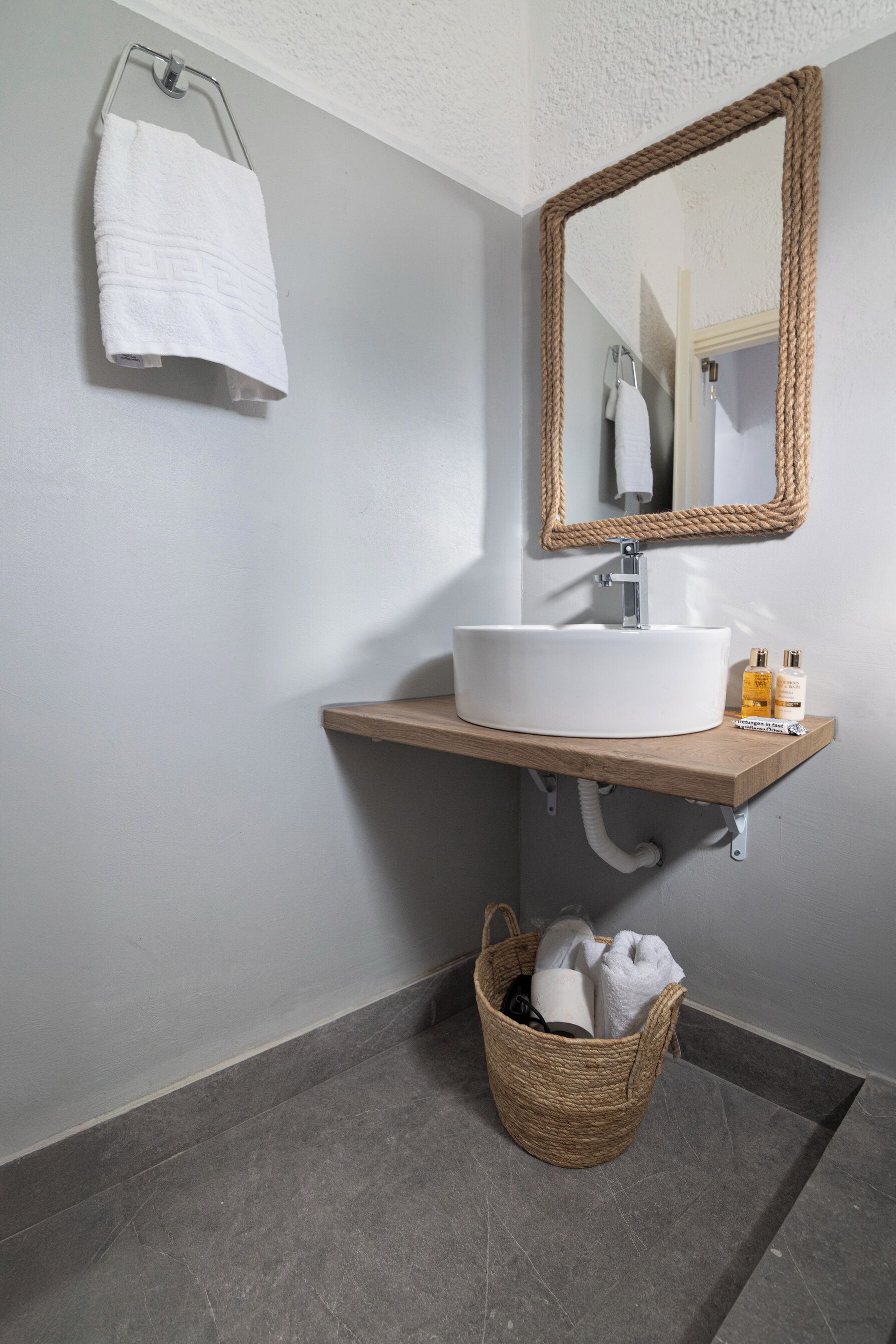 A bathroom with a white sink, wooden countertop, and a woven basket under the sink.