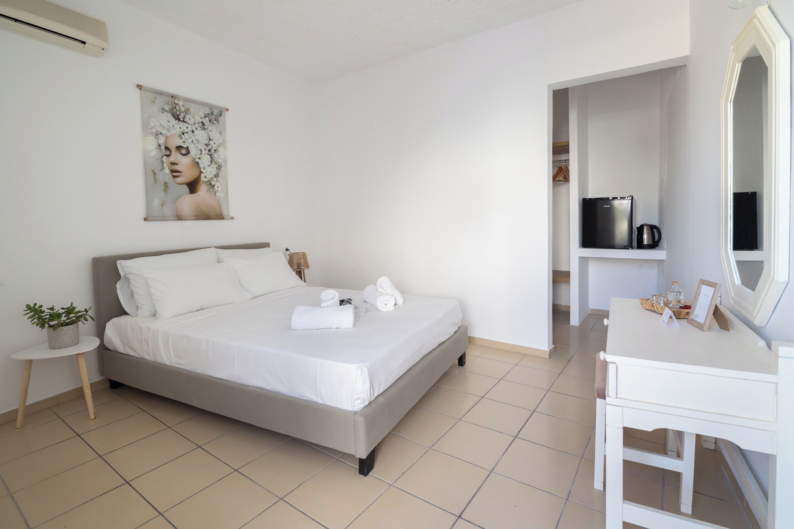 A bedroom with a bed, a small bedside table with a plant, a white dresser, and a mirror.