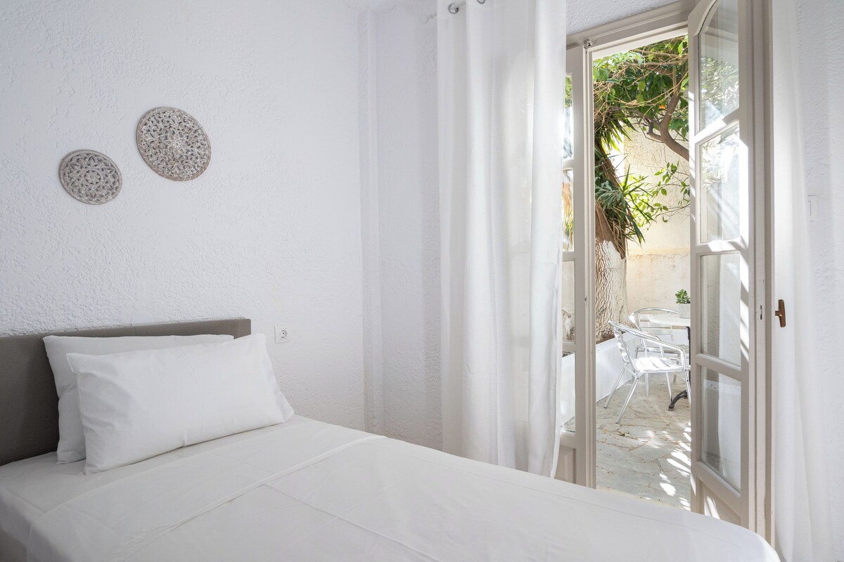 A bedroom with a bed, a window with curtains, and a view of an outdoor patio area.