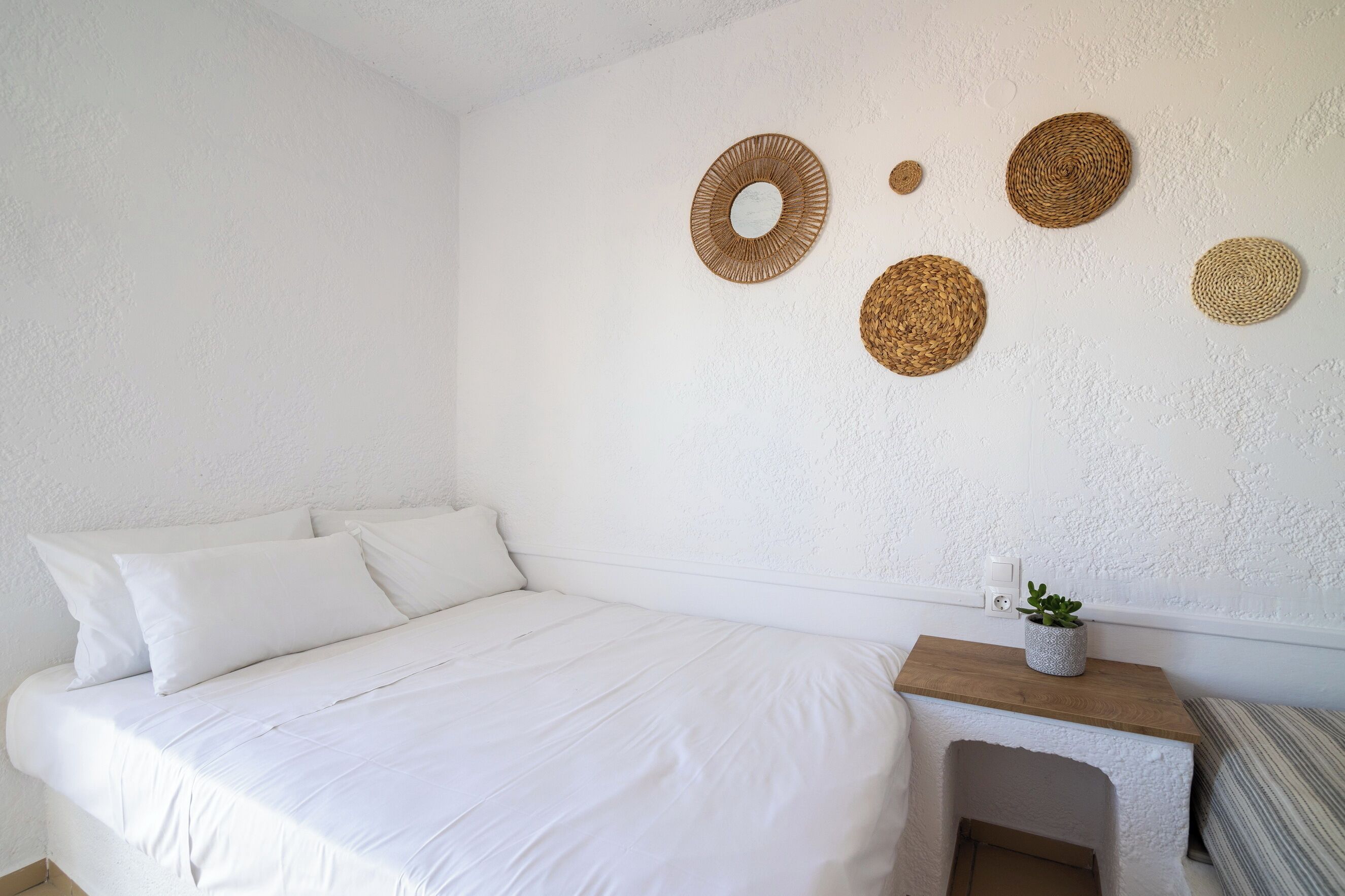 A bedroom with a large bed, a bedside table with a plant, and decorative woven wall art.