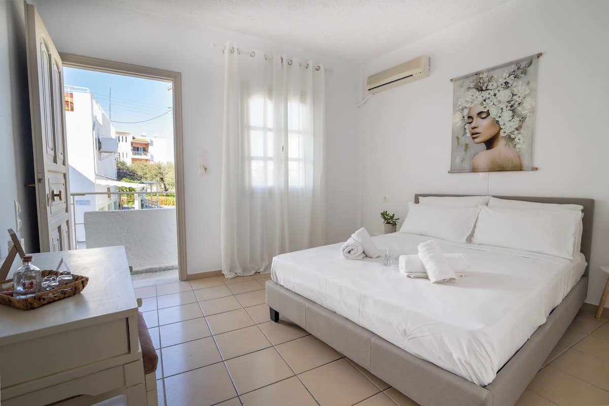 A hotel room with a bed, a desk, a window with curtains, a wall-mounted air conditioner, and a painting.