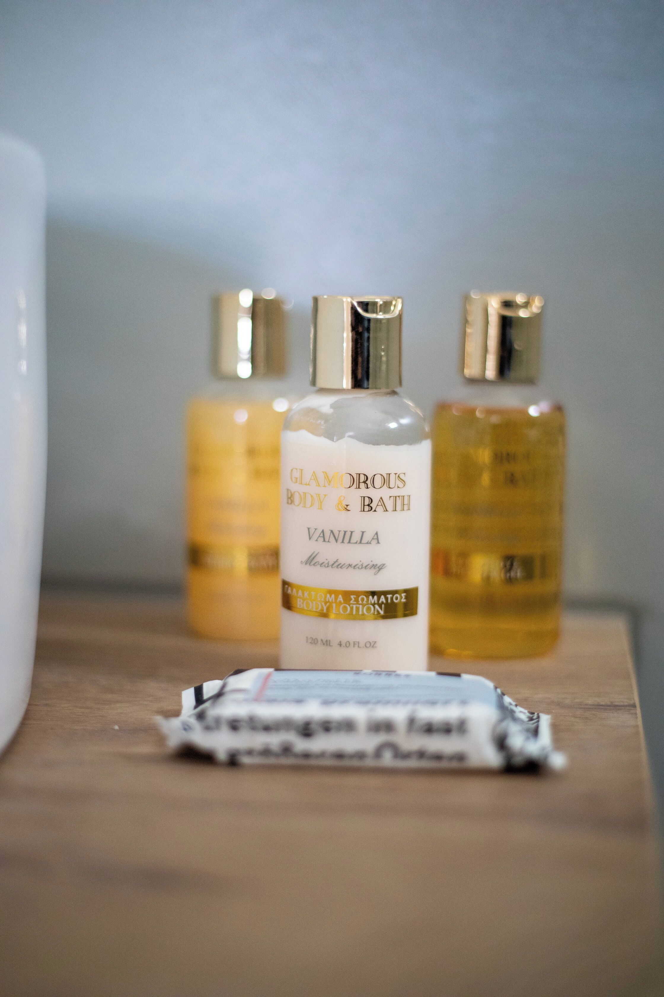 Three bottles of Glamorous Body & Bath Vanilla body lotion on a wooden surface.