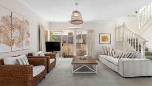 A spacious living room with a large TV, wicker furniture, a white sofa, and a staircase. - The Lighthouse Point Lonsdale (Point Lonsdale)