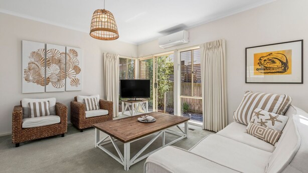 A living room with a TV, wicker furniture, a wooden coffee table, and artwork. - The Lighthouse Point Lonsdale (Point Lonsdale)
