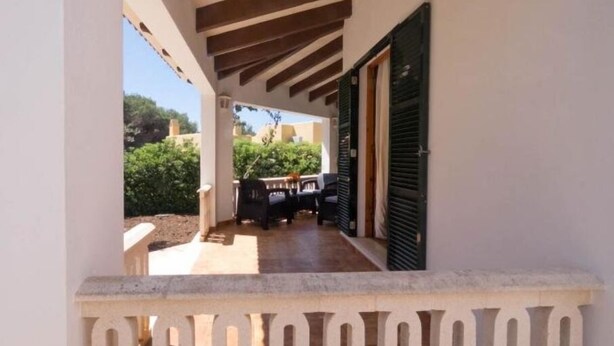 Ein überdachter Außenbereich mit Patio-Tisch und -Stühlen, einer Holzbalkendecke und einer grünen Rolltür.