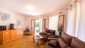 Ein Wohnzimmer mit einer Sofagarnitur, einem Couchtisch, einem Fernseher auf einem Schrank und einer Pflanze.