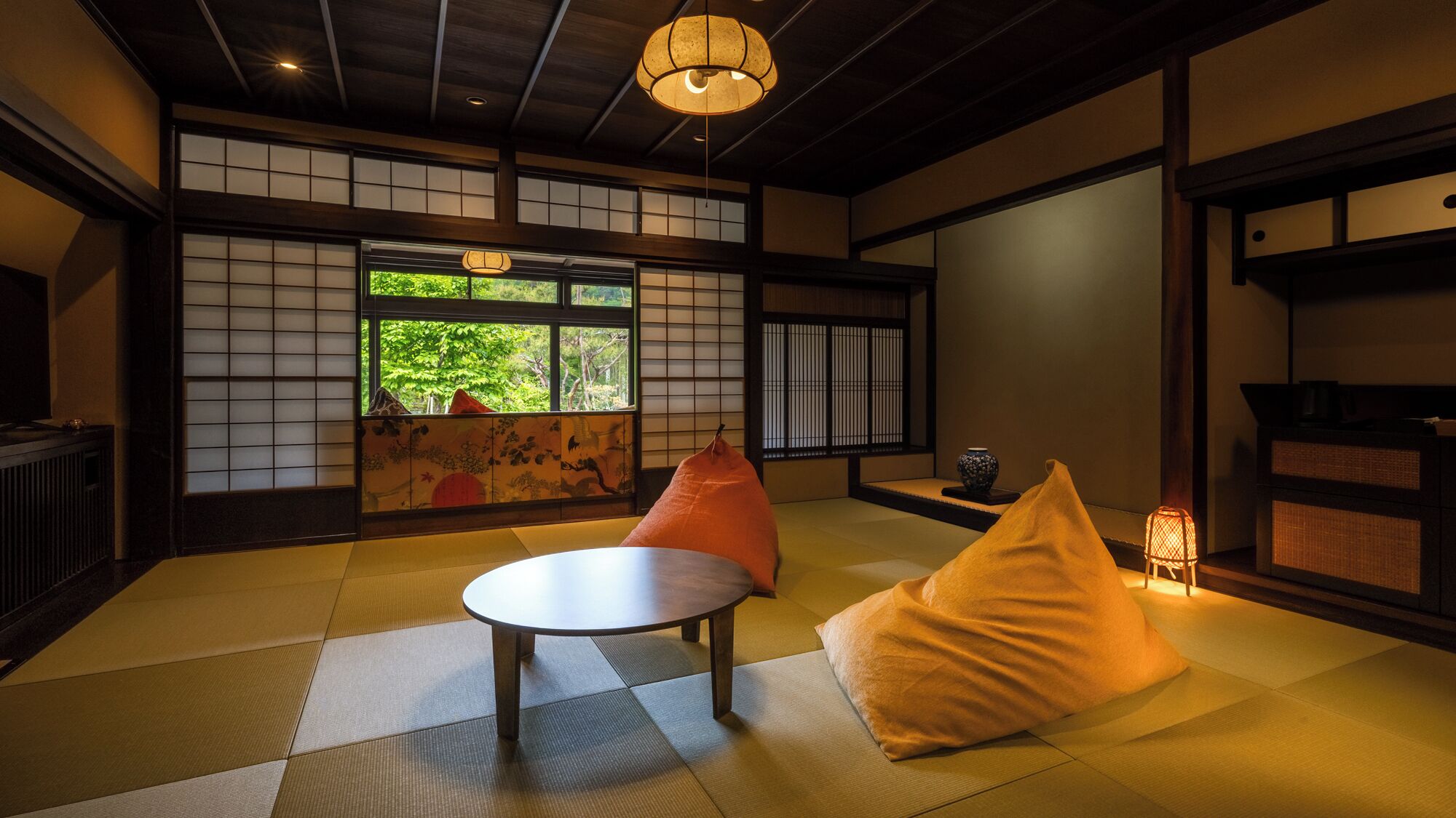 Ein traditioneller japanischer Raum mit Tatami-Boden, einem niedrigen Tisch, Kissen und Blick ins Grüne durch Shoji-Schirme.
