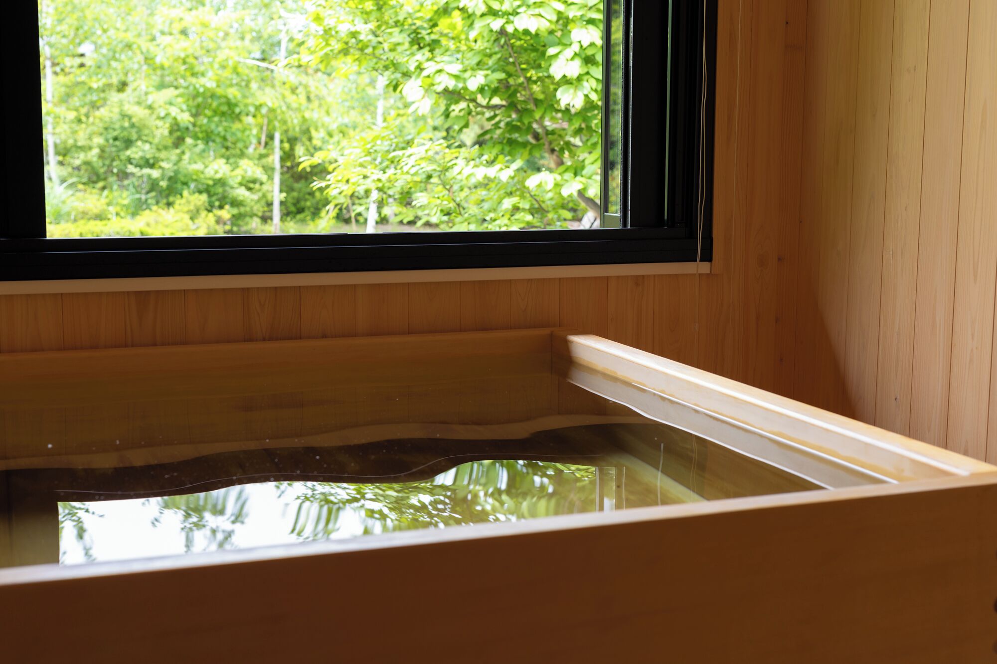 Una bañera de madera con ventana que refleja follaje exterior.