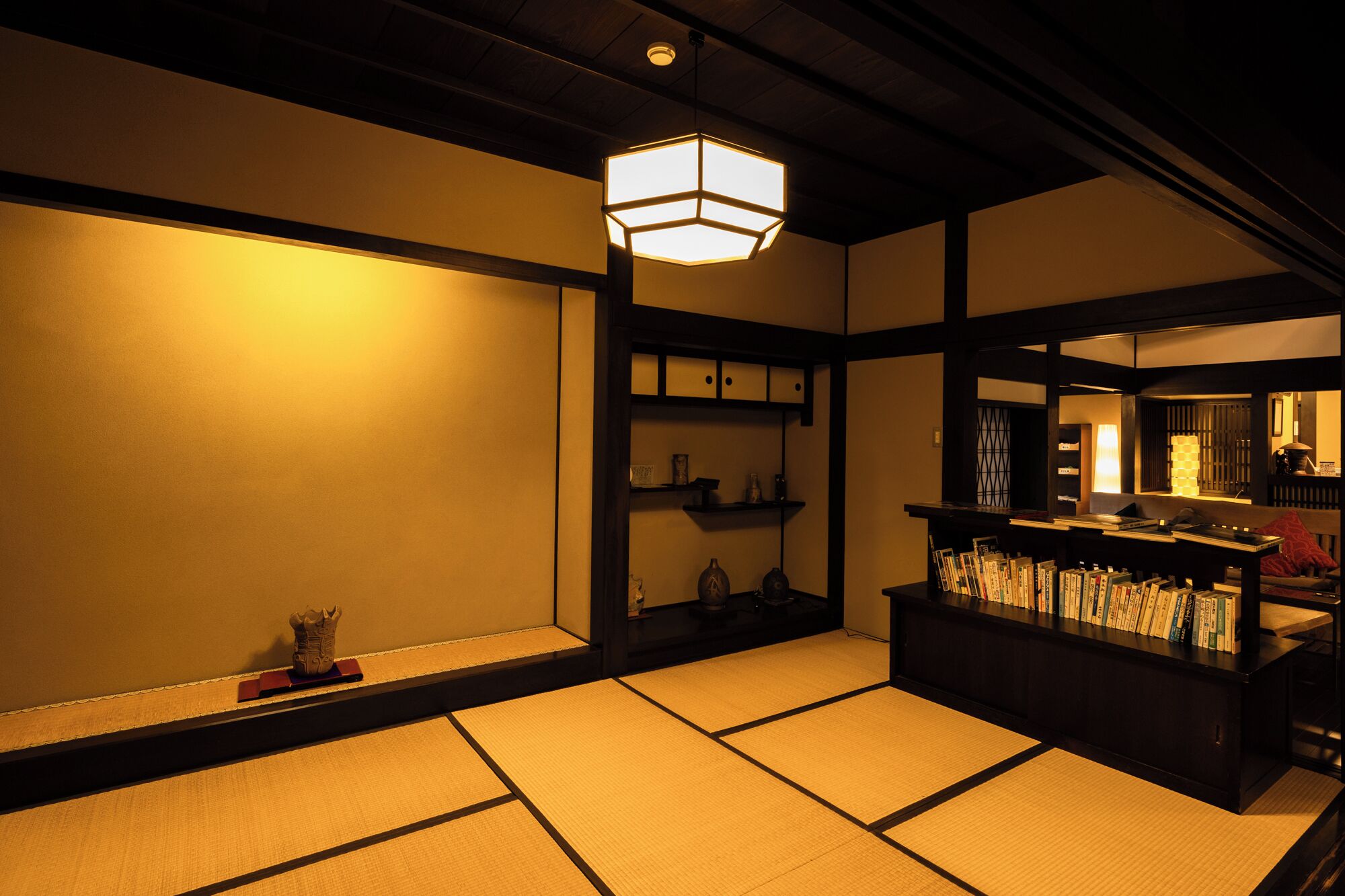 A traditional Japanese room with tatami flooring, a low wooden desk with books, and a hanging light fixture.