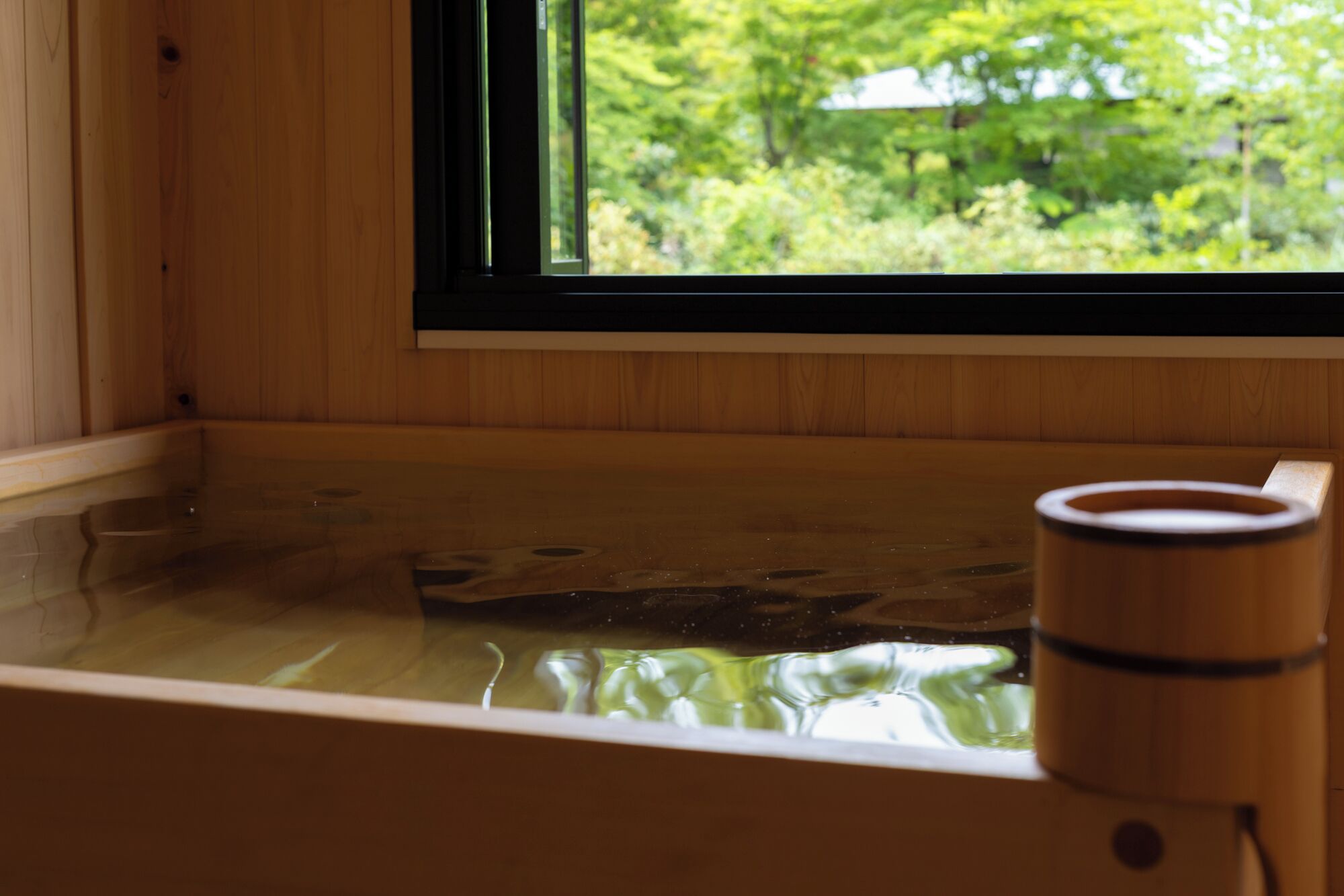 A wooden cabin with a hot tub and a window overlooking greenery.