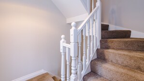 Un escalier avec des balustrades blanches et des marches recouvertes d’une moquette marron.
