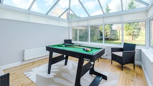 Une table de billard dans une pièce baignée de lumière, avec de grandes fenêtres donnant sur l’extérieur.